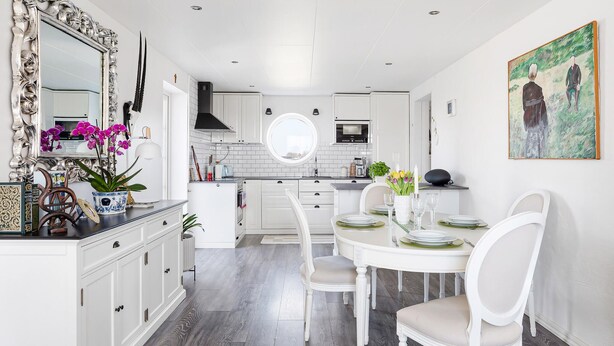 A modern kitchen with white cabinetry, a central island, and a dining area with white chairs and a round table. - 3 bedroom cozy home in Tomelilla (Tomelilla)