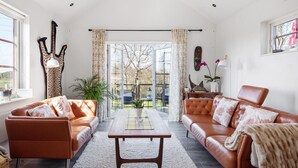 A spacious living room with leather sofas, a wooden coffee table, and a view of a garden through large glass doors. - 3 bedroom cozy home in Tomelilla (Tomelilla)