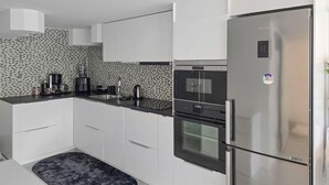 A modern kitchen with white cabinets, a stainless steel refrigerator, a built-in oven, and a coffee maker.