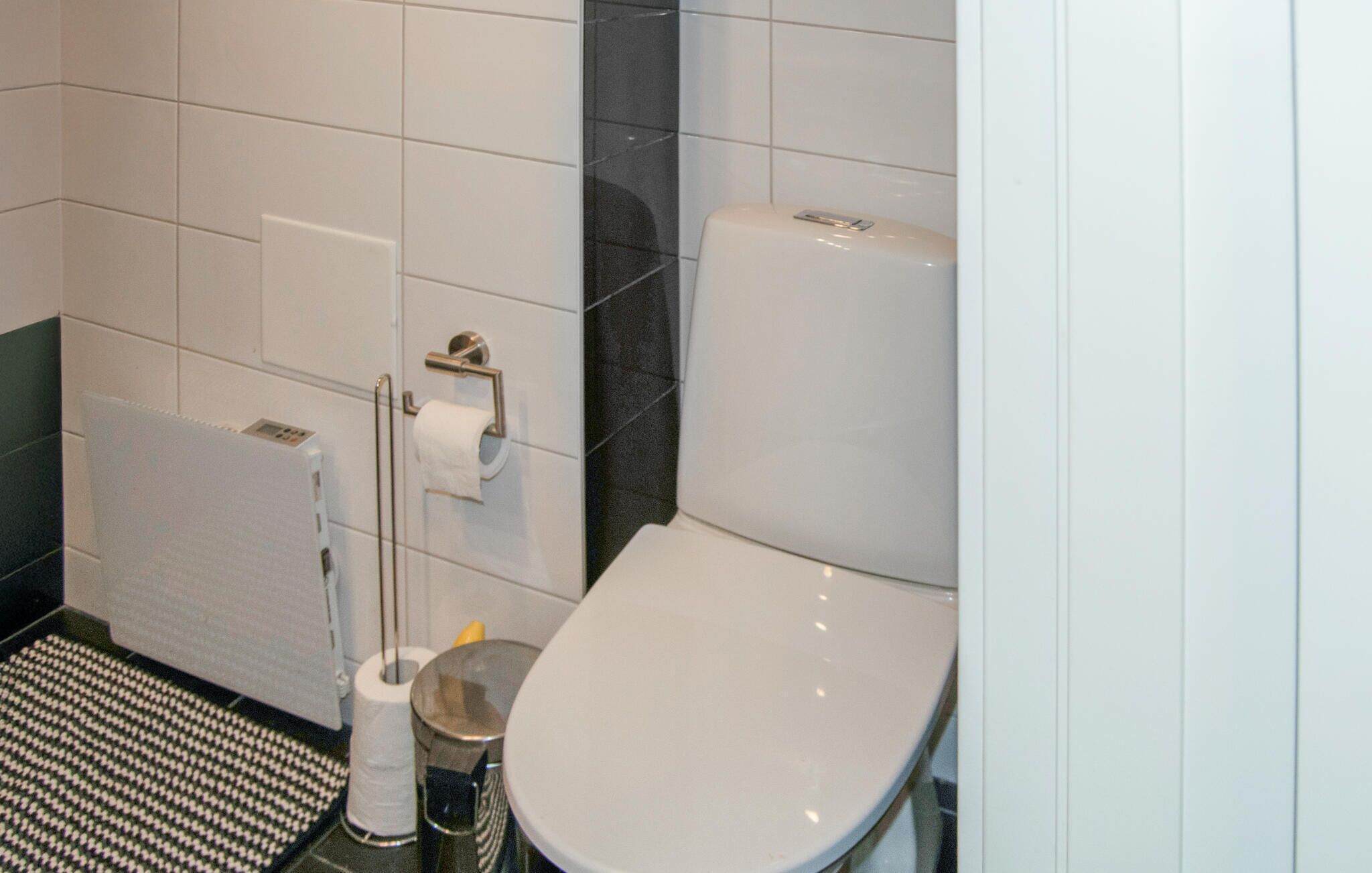 Une salle de bain avec des toilettes blanches, un distributeur d’essuie-tout, un rouleau de papier toilette et un sèche-mains.