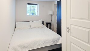 A bedroom with a bed, a window, a lamp, and a door.