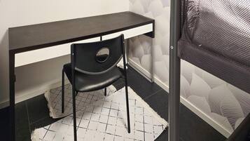 A small, dark-colored desk with a chair in front, a patterned rug, and a mesh screen door.