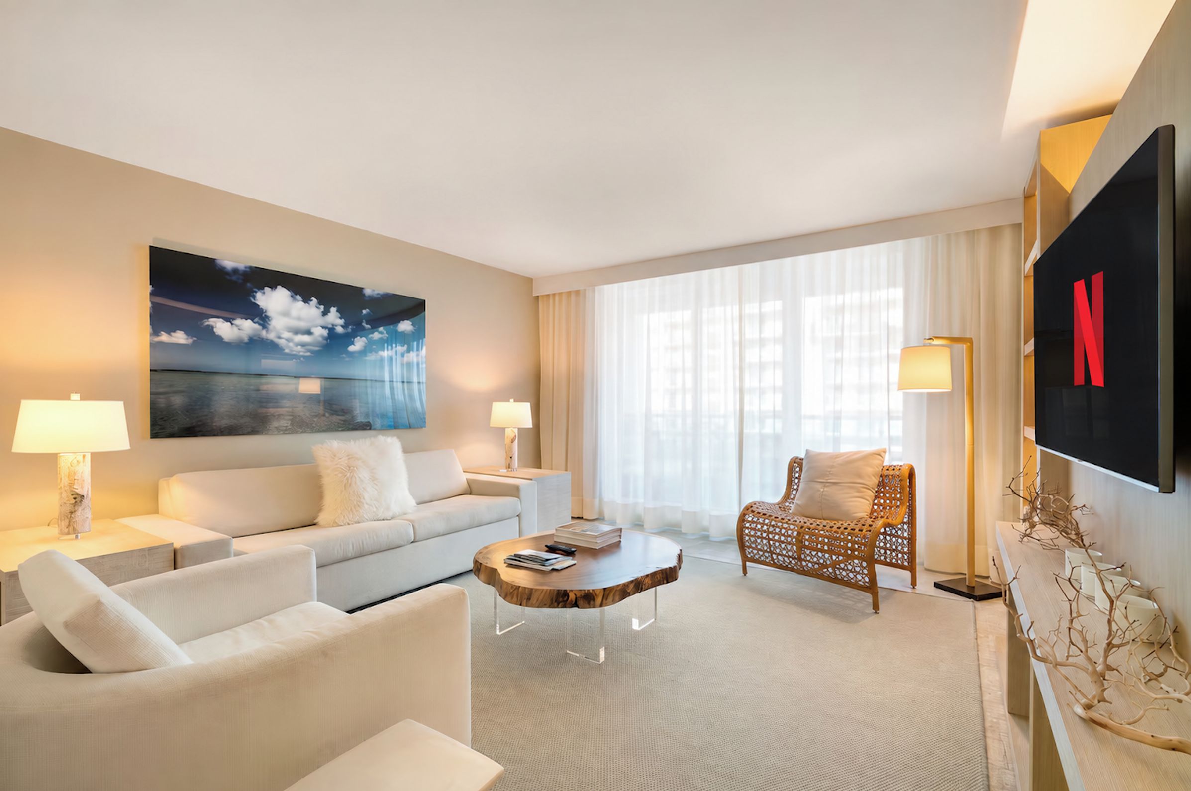 A modern hotel room with a large flat-screen TV, a comfortable sofa, a wooden coffee table, and a decorative chair.