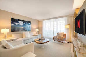 A modern hotel room with a large flat-screen TV, a comfortable sofa, a wooden coffee table, and a decorative chair.