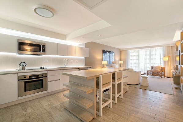 Een moderne keuken met ingebouwde apparatuur, een eethoek met een bar, en een woongedeelte met een bank en een groot raam.