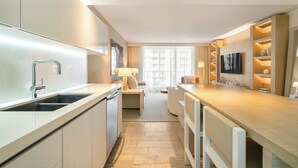 A modern hotel kitchen with a central island, a built-in sink, and a flat-screen TV mounted on the wall.