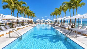 Resort-style oceanfront pool with palm-lined loungers and sunny tropical views