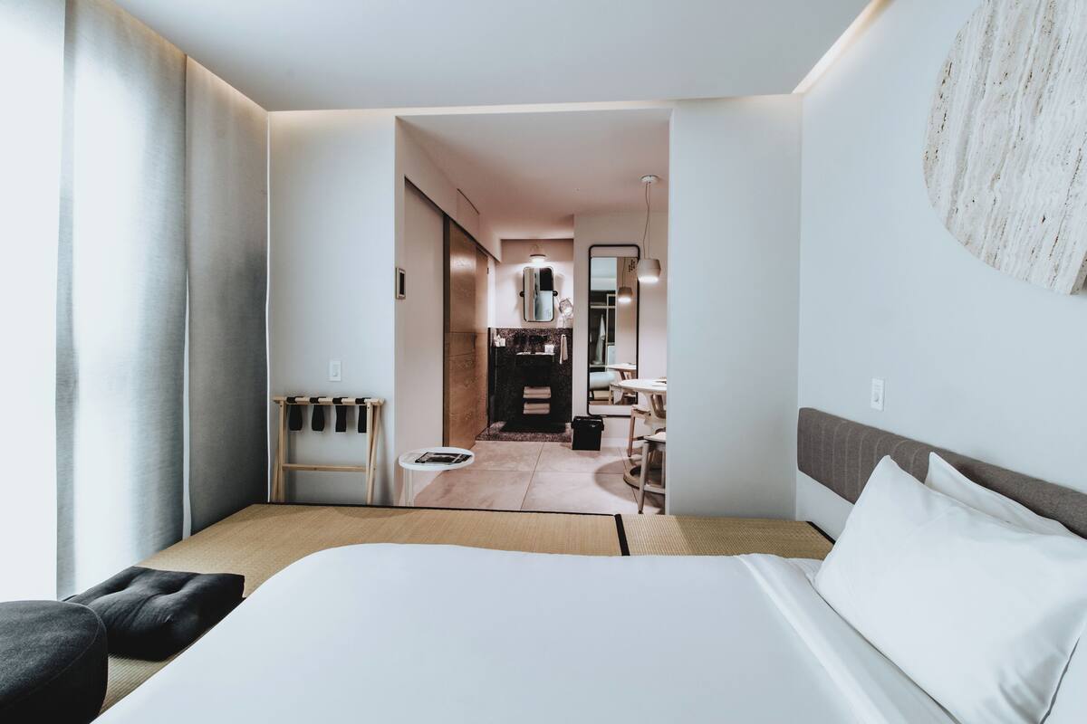 Moderni hotellihuone, jossa on suuri sänky, pieni pöytä ja näkymä keittiötilaan.