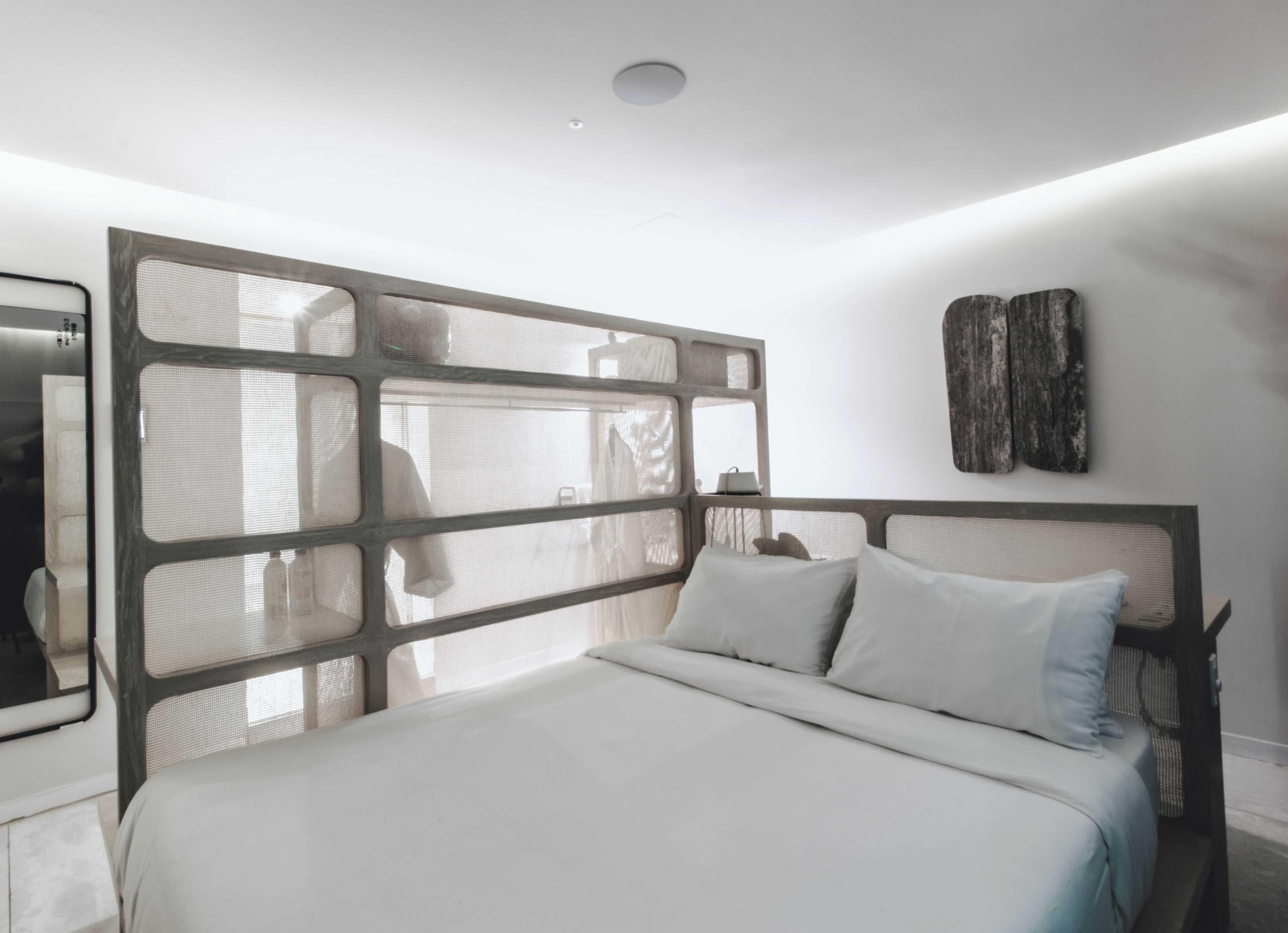 A modern bedroom with a large bed, a headboard with a geometric design, and a wall-mounted artwork.