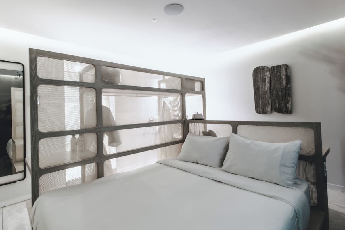 A modern bedroom with a large bed, a headboard with a geometric design, and a wall-mounted artwork.