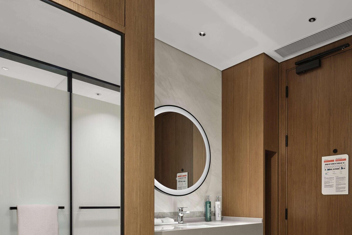A modern bathroom with a wooden vanity, a large mirror, and a glass shower enclosure.