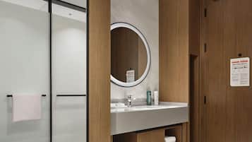 A modern bathroom with a wooden vanity, a large mirror, and a glass shower enclosure.