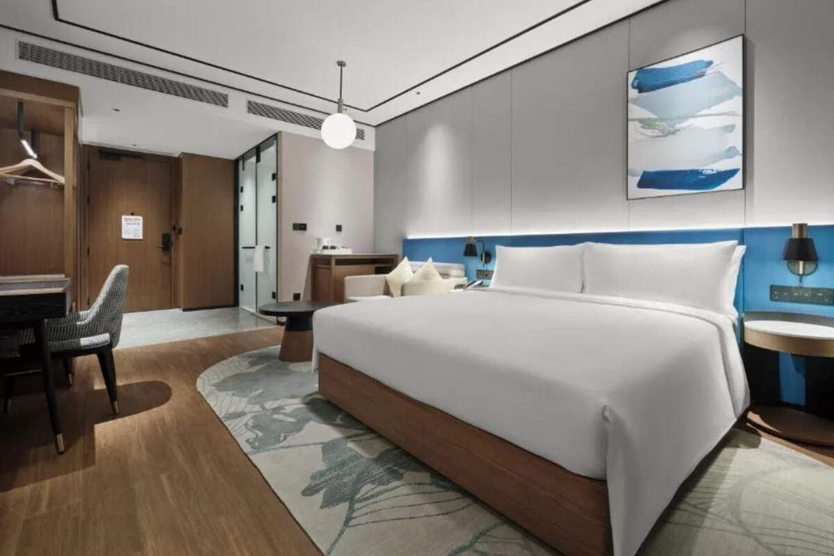 A modern hotel room with a large bed, a desk, and a chair.