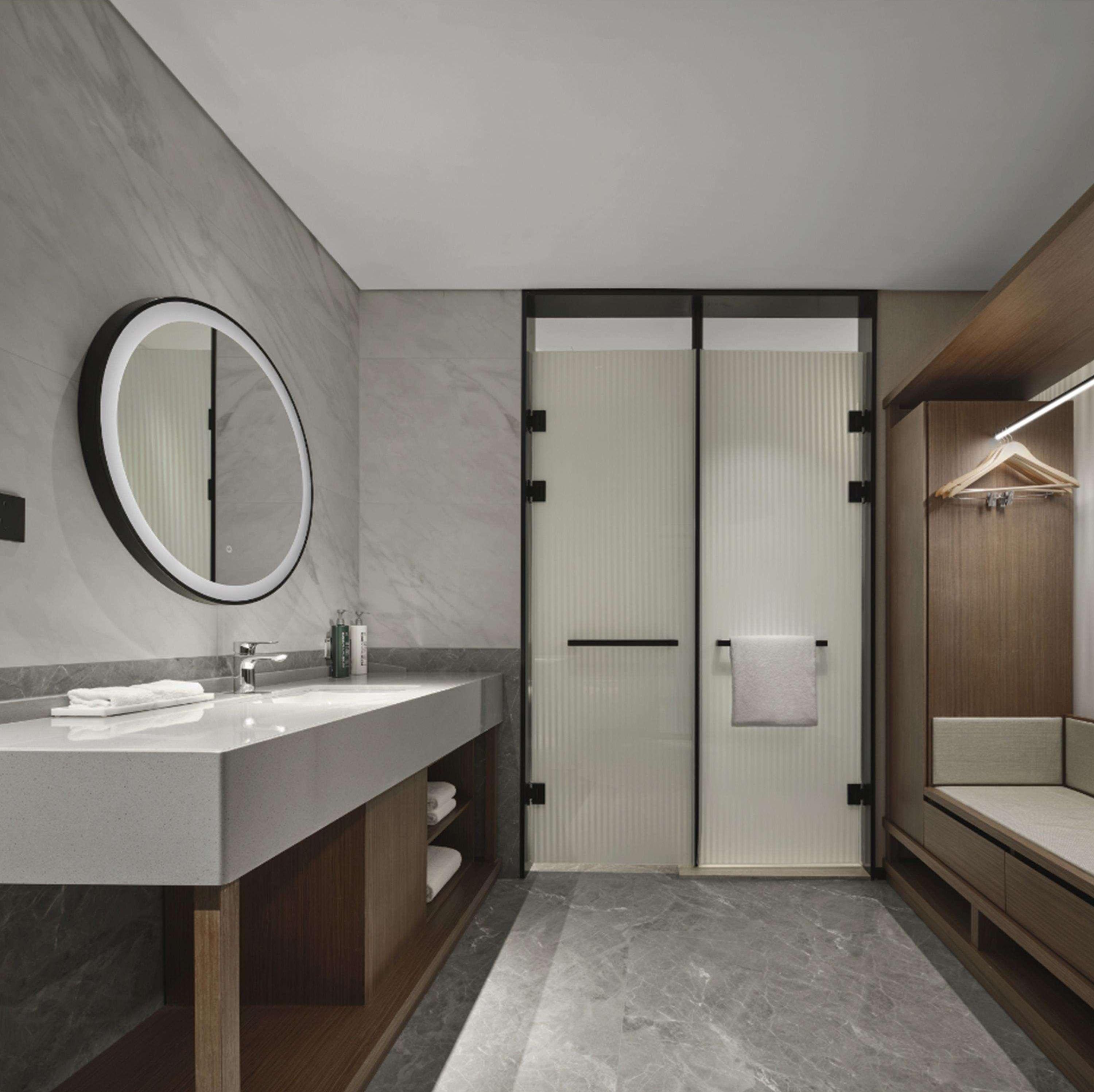 A modern bathroom with a marble vanity, a large mirror, and a walk-in shower with a towel hanging on the door.