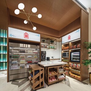 Un espacio comercial moderno con un mostrador central, una vitrina refrigerada para bebidas y estantes llenos de aperitivos y productos envasados.