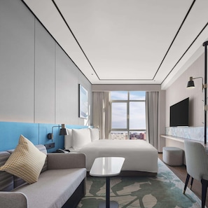 Een moderne hotelkamer met een bed, een bank, een klein tafeltje, een televisie en een raam met uitzicht op de stad.