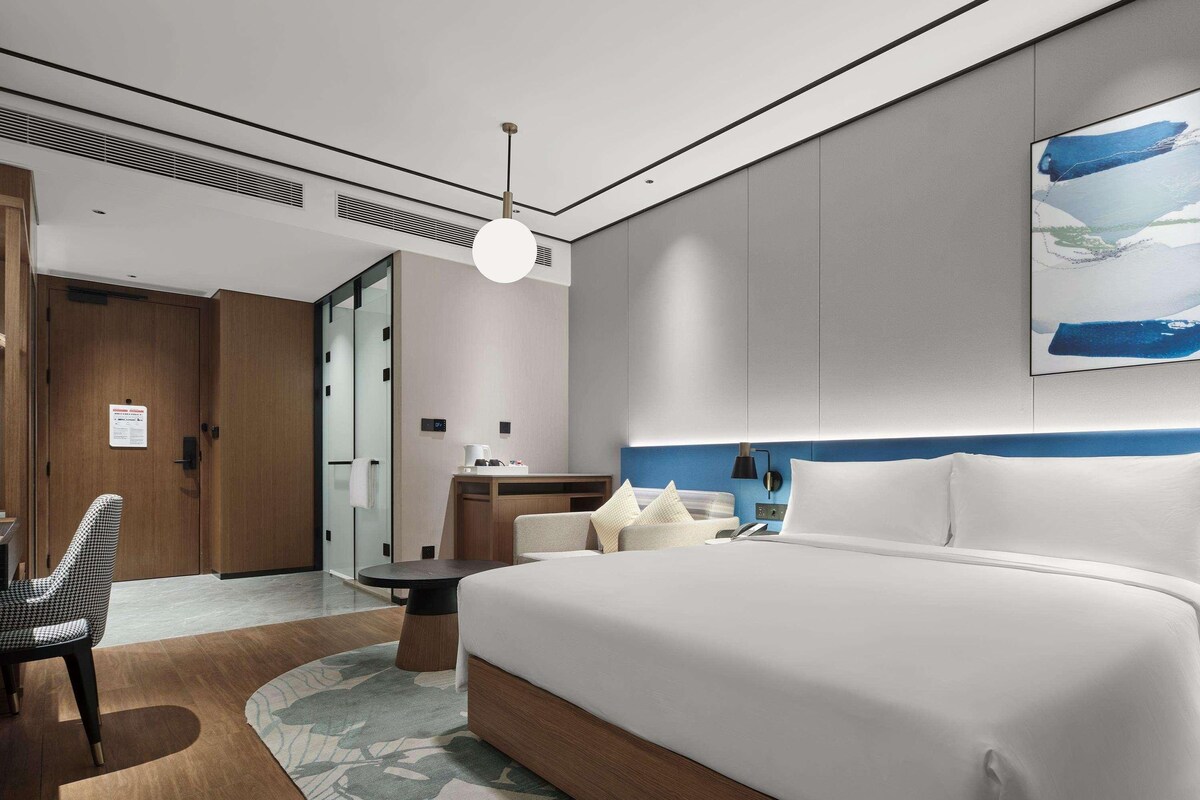 A modern hotel room with a large bed, a desk, and a chair.