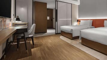 A modern hotel room with a wooden desk, two beds, a chair, and a large mirror.