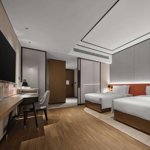 Una habitación de hotel moderna con un escritorio de madera, dos camas, una silla y un espejo grande.