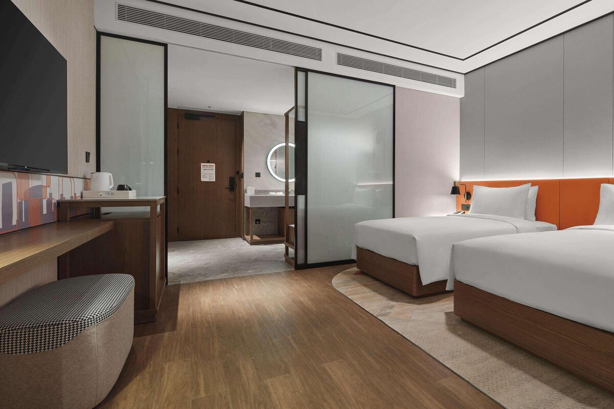 Een moderne hotelkamer met een houten bureau, een bed met wit beddengoed, een grote spiegel en een aparte badkamer.