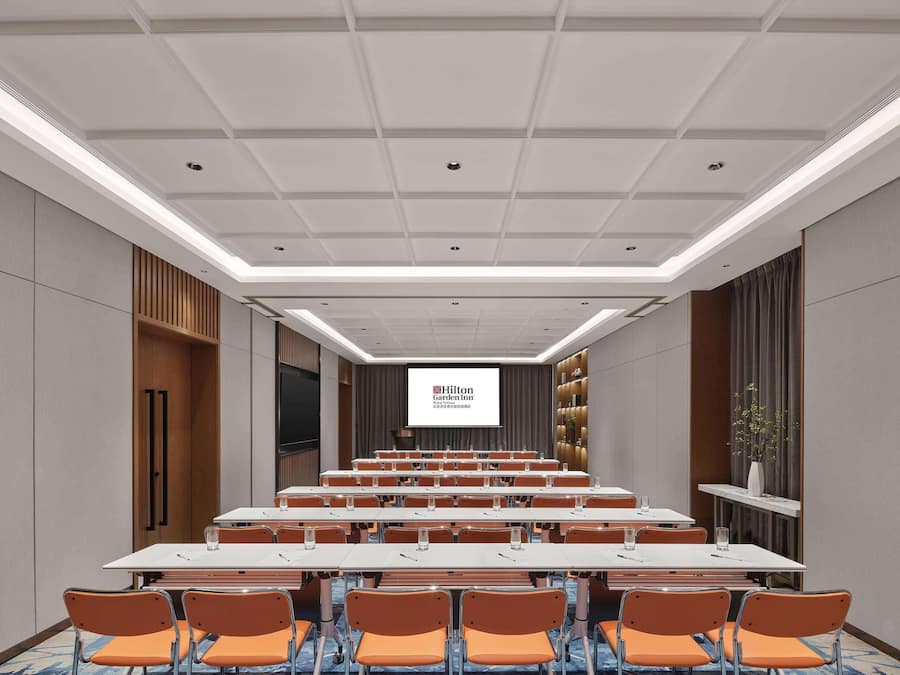 A conference room with a long table, orange chairs, and a screen displaying Hilton Garden Inn.