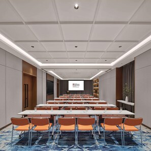 Een vergaderruimte met een lange tafel, oranje stoelen en een scherm waarop Hilton Garden Inn staat.