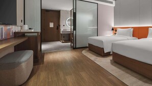 Une chambre d’hôtel moderne avec un bureau en bois, un lit avec une literie blanche, un grand miroir et une salle de bain séparée.