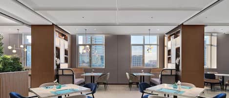 A modern dining area with multiple tables and chairs, large windows with city views, and a high ceiling with recessed lighting.