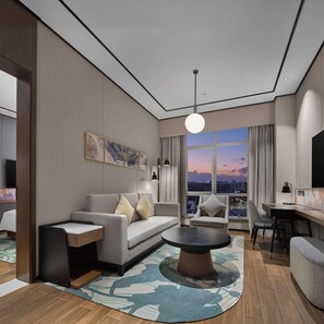 Habitación de hotel moderna con un sofá gris, una mesa de centro y vistas a la ciudad a través de amplias ventanas.