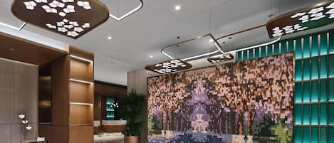 A modern lobby with geometric ceiling lights, a reception desk, and a colorful mosaic wall.
