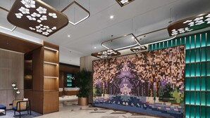 Un hall d’entrée moderne avec des luminaires au plafond aux formes géométriques, un comptoir d’accueil et un mur décoré d’une mosaïque colorée.