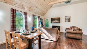 A cozy living room with a wooden ceiling, a dining area with wooden chairs, a sofa, and a fireplace.
