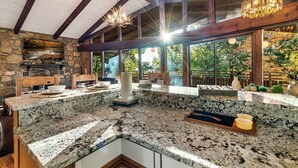 Una cocina con encimeras de granito, chimenea de piedra, vigas de madera y ventanas amplias con vistas a un jardín.