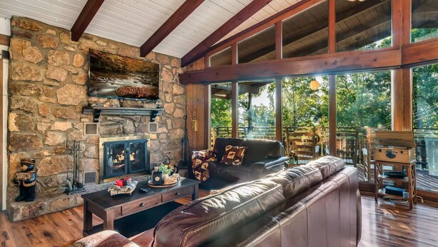 Una sala de estar acogedora con chimenea de piedra, sofá de cuero y grandes ventanales con vistas al exterior.