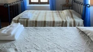 Una stanza con due letti, una finestra con tende, un termosifone e un piccolo tavolo con una lampada.