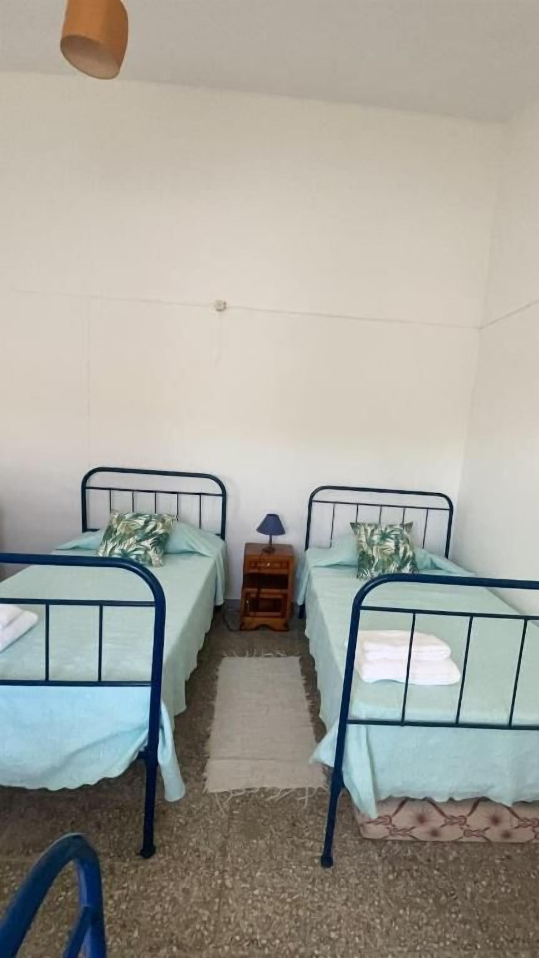 Una habitación con dos camas individuales, una mesita de noche de madera, una lámpara y un suelo sencillo.