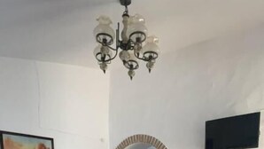 Zona pranzo con tavolo ricoperto da una tovaglia a quadri, un divano con cuscini a righe, una sedia di legno e un lampadario.