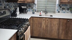 Una cucina moderna con mobili in legno, un piano cottura in acciaio inossidabile, un forno a microonde e una finestra con persiane.