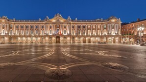 Un edificio histórico imponente con fachada simétrica, una entrada central amplia y un espacioso patio con diseños geométricos en el pavimento.