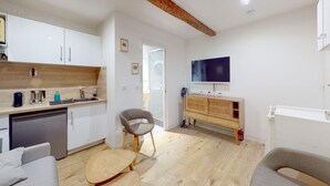 Una cocina compacta con gabinetes blancos, encimera de madera, lavavajillas integrado y una silla gris.