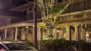 A building with a tree wrapped in lights, a parked car, and a balcony with railings. - Olde Naples beautiful Condo Steps to Pier, Beach, Sunsets and restaurants!  (Naples)