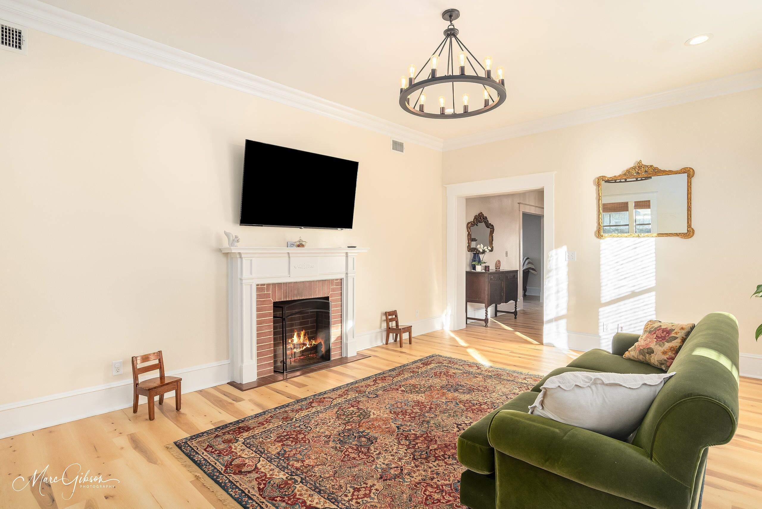 A living room with a fireplace, a television mounted above it, a green sofa, and a patterned rug.