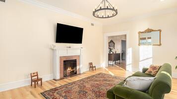 A living room with a fireplace, a television mounted above it, a green sofa, and a patterned rug.