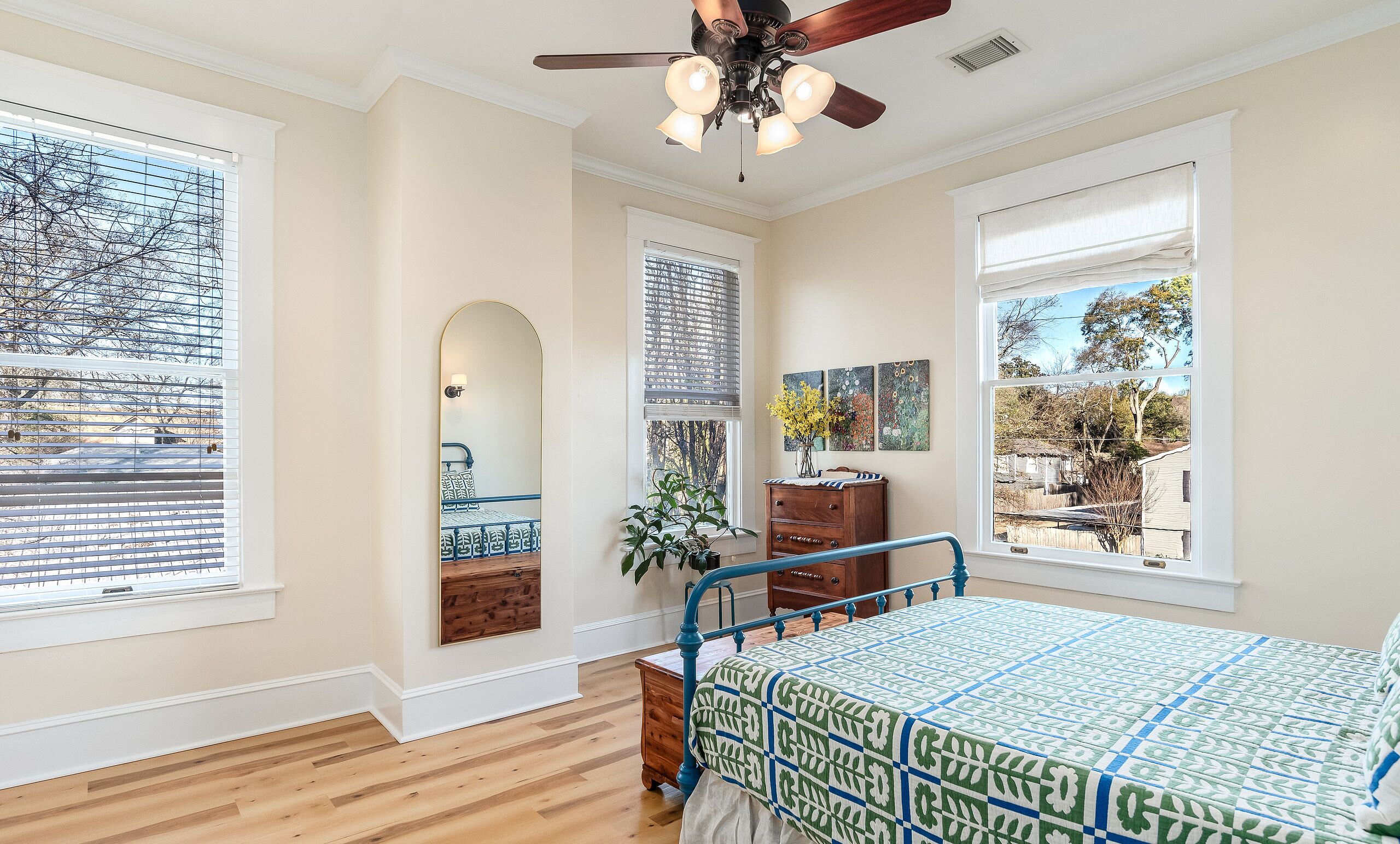A bedroom with a bed, a dresser, a mirror, and a ceiling fan.