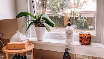 A bathroom with a sink, a potted plant, a bottle of hand cream, and a shelf with bottles.