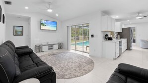 A spacious living room with a black sofa, a round rug, and a TV on the wall. - Family house  4 bedrooms 3 bath sleeps 12. 2 master suites Naples heated pool (Naples)