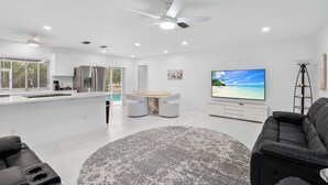 A modern living space with a kitchen, dining area, and a large flat-screen TV. - Family house  4 bedrooms 3 bath sleeps 12. 2 master suites Naples heated pool (Naples)