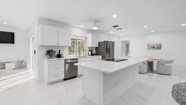 A modern kitchen with white cabinetry, a central island, stainless steel appliances, and a dining area with a gray sofa. - Family house  4 bedrooms 3 bath sleeps 12. 2 master suites Naples heated pool (Naples)