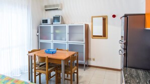Une petite pièce avec une table et des chaises en bois, un panier bleu, un appareil de climatisation blanc, une petite télévision et un réfrigérateur.
