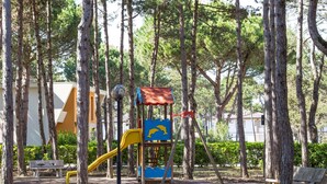 Un terrain de jeux avec un toboggan et une structure d’escalade, entouré d’arbres et de bancs.